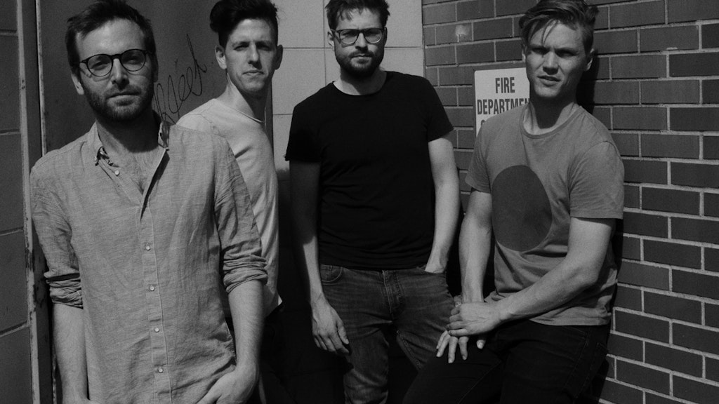 Les quatre membres du groupe Ensemble Nikel se tiennent devant un mur de briques.