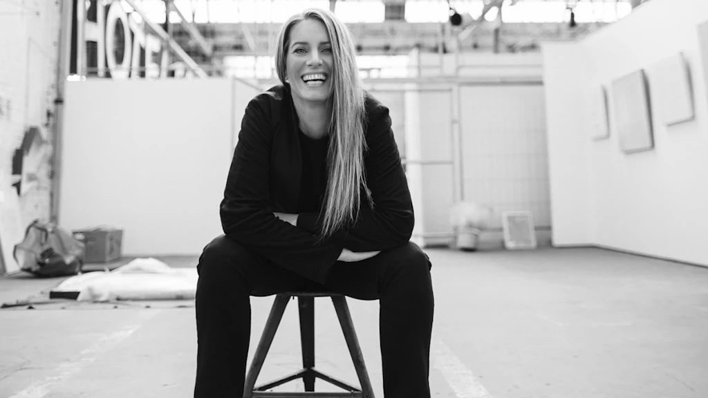 Ritratto di Sonja Moonear. È seduta su uno sgabello, è chinata in avanti in modo rilassato e offre un ampio sorriso alla fotocamera.