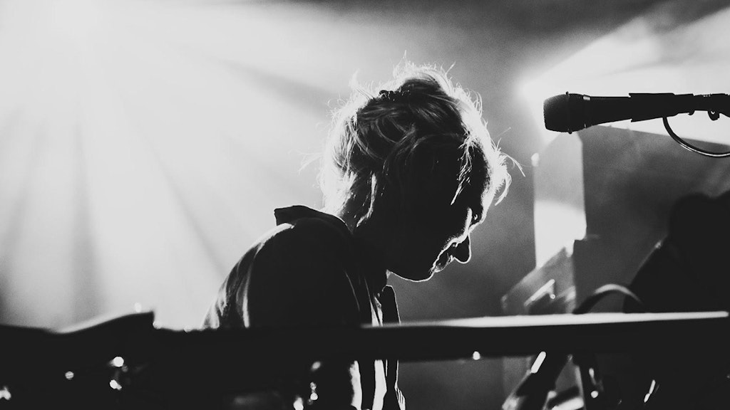 Black and white photo of Simone Aubert. There are instruments in the foreground, Simone is half-turned away looking at another instrument.