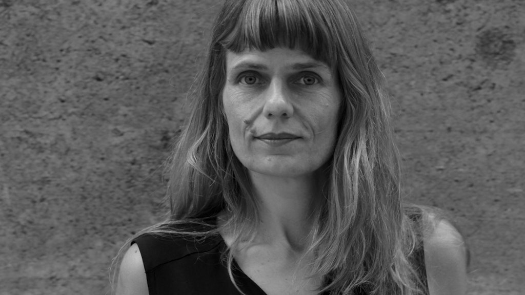 Portrait de Katharina Rosenberger. Elle se tient devant un mur en béton et regarde la caméra avec un sourire réservé.