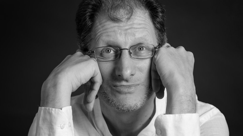Black and white photograph of Ivo Antognini. He holds his head in both hands and looks into the camera.