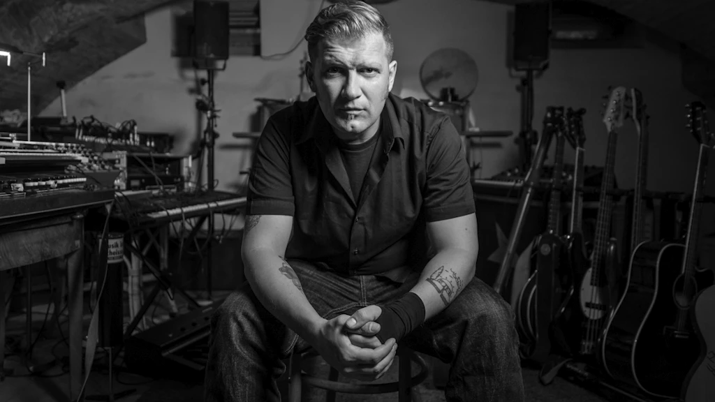 Ritratto di Mario Batkovic. È seduto su una sedia e guarda direttamente nell’obbiettivo della fotocamera. Sullo sfondo c'è una moltitudine di strumenti.