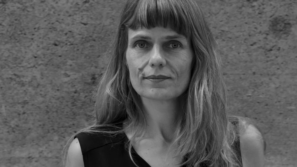 Ritratto di Katharina Rosenberger. Si trova di fronte a un muro di cemento e guarda nell’obbiettivo della fotocamera offrendo un sorriso riservato.