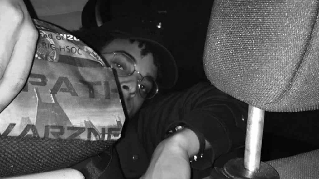 Scatto in bianco e nero di Tapiwa Svosve che guarda la fotocamera dal retro di un'auto, tra i poggiatesta. 