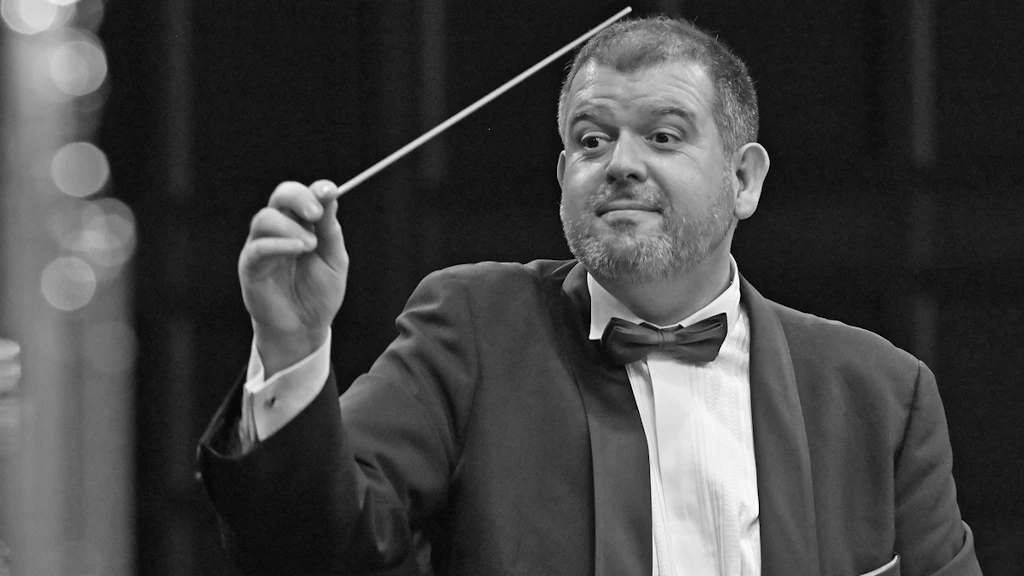 Carlo Balmelli dirige con la bacchetta sollevata.