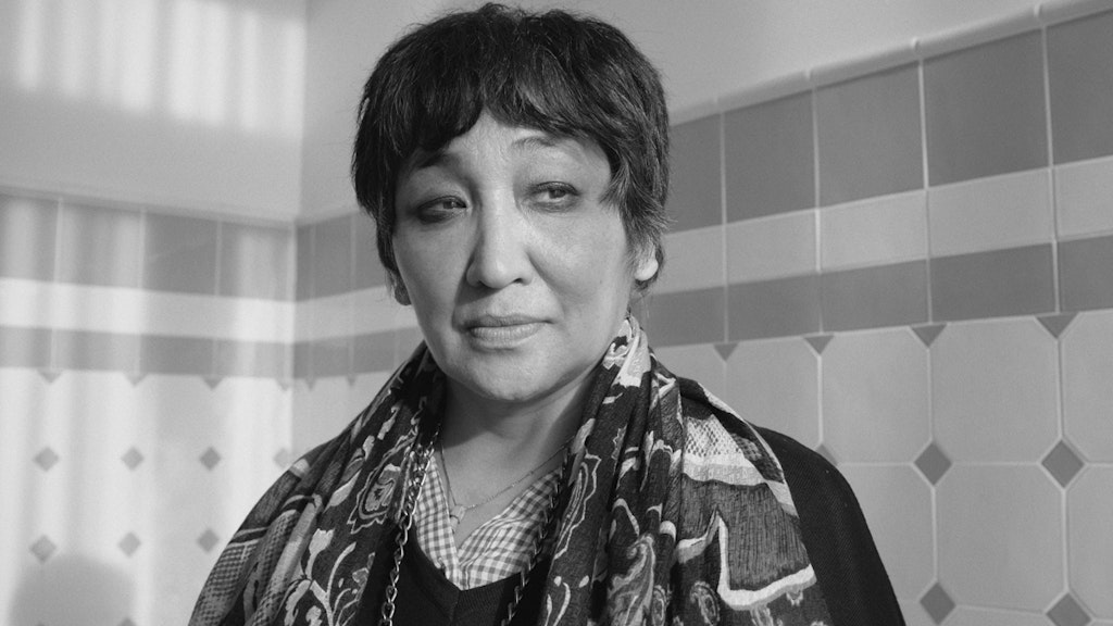 Portrait de Saadet Türköz. Elle se tient devant un mur décoré de carreaux de faïence.