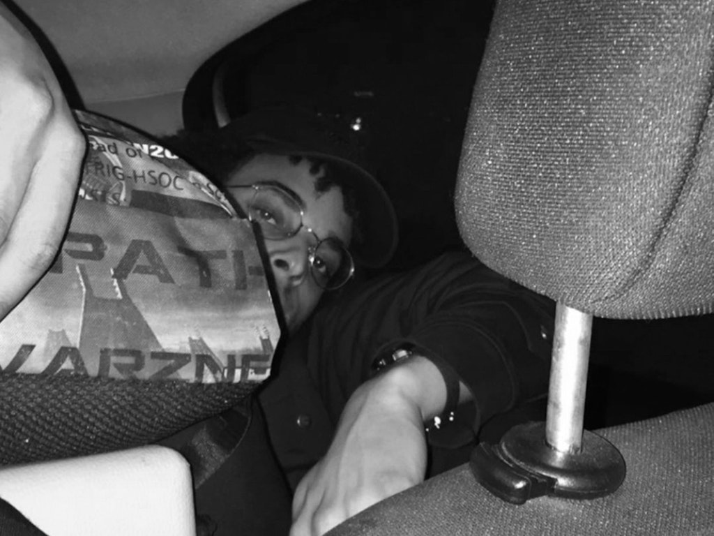 Black-and-white photograph of Tapiwa Svosve looking into the camera from the backseat of a car.