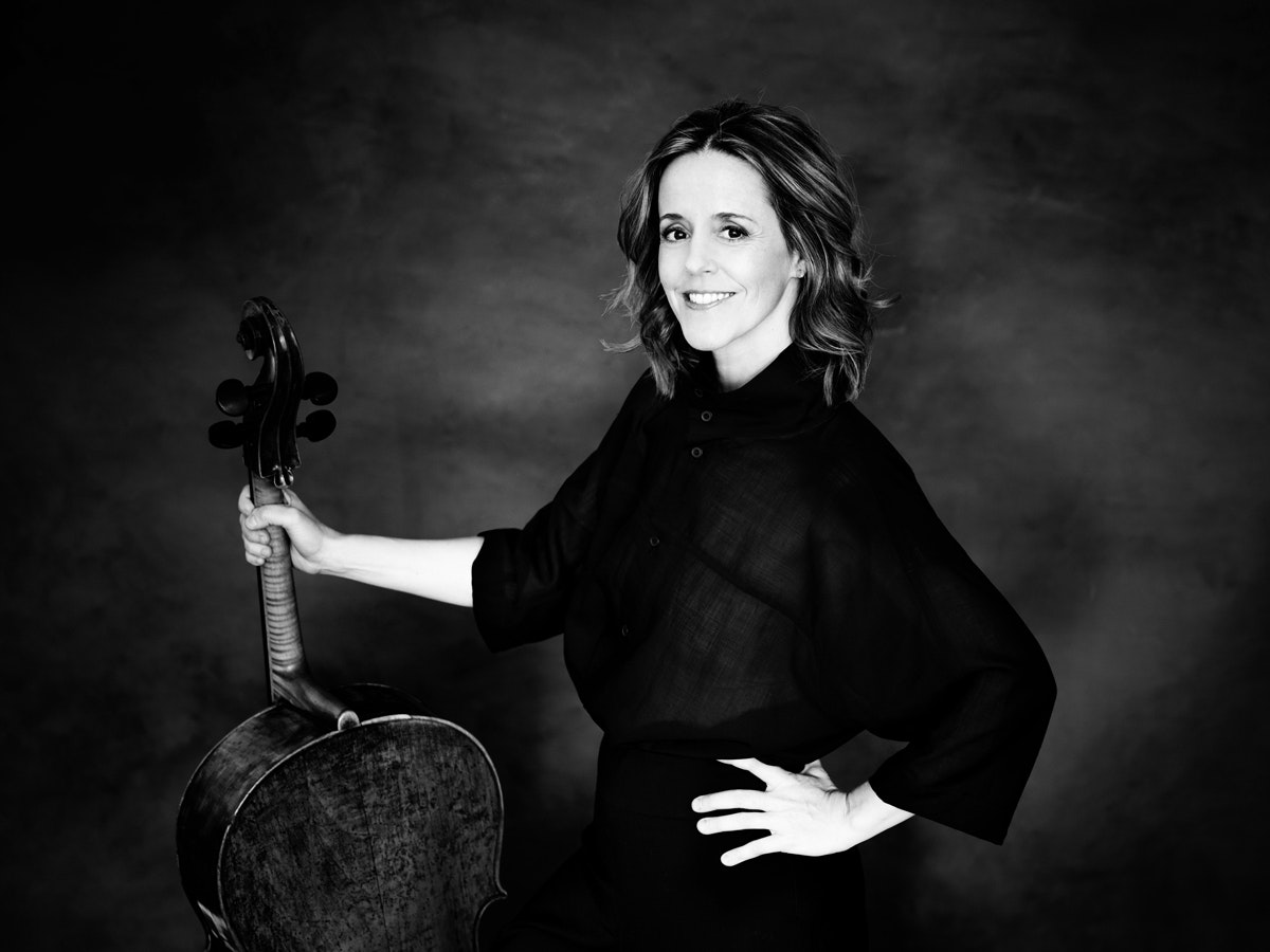 Photo en noir et blanc de Sol Gabetta tenant son violoncelle et regardant la caméra en souriant.