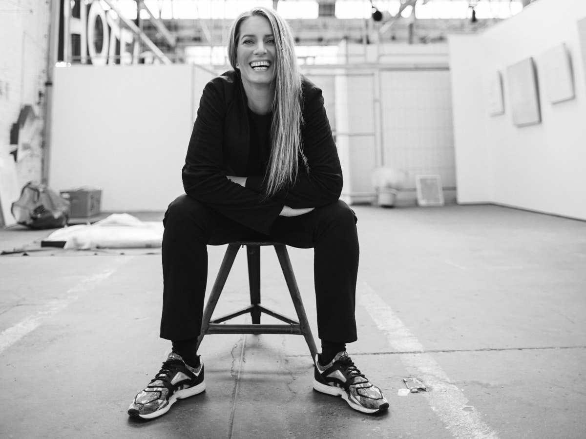 Portrait de Sonja Moonear. Elle est assise sur un tabouret, détendue, penchée en avant et rit un grand rire à la caméra.