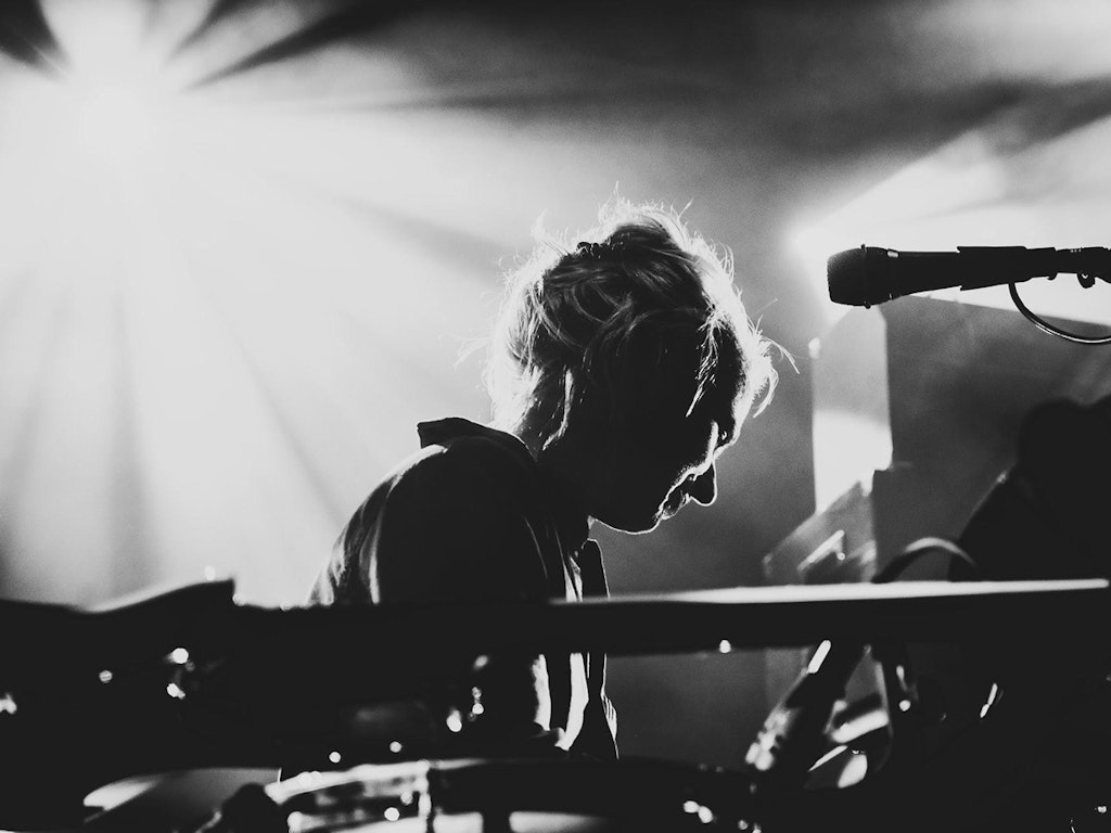 Photo en noir et blanc de Simone Aubert. Des instruments sont placés au premier plan, Simone regarde un autre instrument en se détournant à moitié.