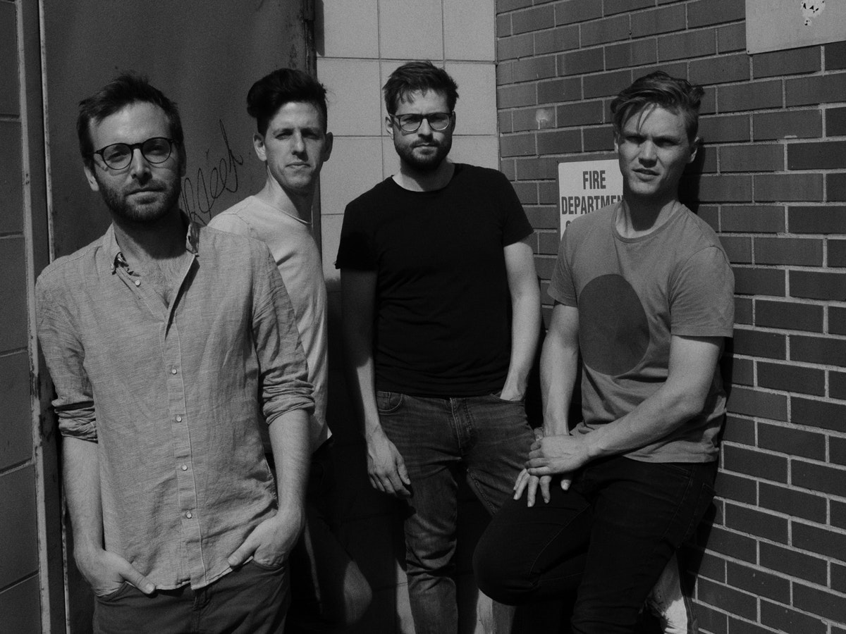 Les quatre membres du groupe Ensemble Nikel se tiennent devant un mur de briques.