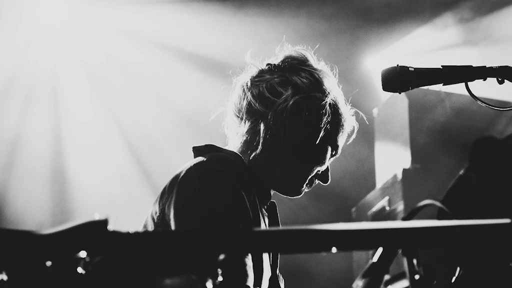Fotografia in bianco e nero di Simone Aubert. Gli strumenti sono posizionati in primo piano, Simone sta guardando un altro strumento, semidistesa.